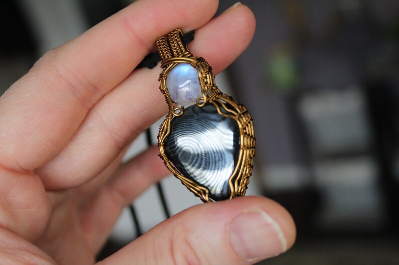 May include: A gold wire wrapped pendant featuring a black and white banded agate stone and a round moonstone.