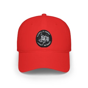 May include: A bright red baseball cap featuring a circular black patch on the front. The patch displays a white graphic of a skull wearing a top hat, surrounded by the text "RESPECT IS EARNED" and "LOYALTY RETURNED" in a circular border.