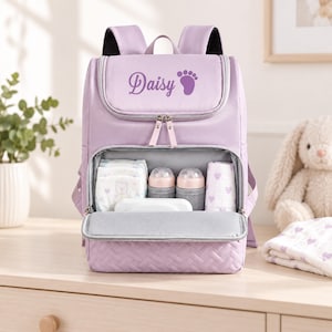 May include: A light purple backpack featuring the name Daisy and a footprint icon printed on the top flap. The open front compartment reveals two baby bottles, a stack of nappies, and a cloth, with a quilted texture on the bottom panel.
