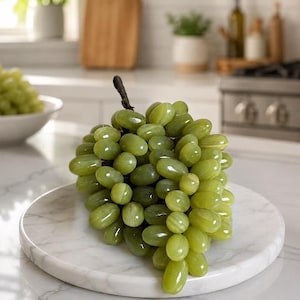 May include: A decorative cluster of artificial grapes crafted from polished light green stone. The individual oval-shaped grapes feature subtle banded patterns and a smooth, glossy finish, attached to a dark, textured stem at the top.