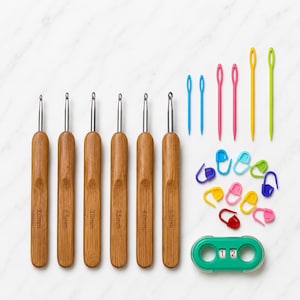 Może przedstawiać: Zestaw sześciu szydełek z bambusowymi rączkami w rozmiarach 2.0mm, 2.5mm, 3.0mm, 3.5mm, 4.0mm i 5.0mm, wraz z sześcioma plastikowymi igłami dziewiarskimi w kolorze niebieskim, różowym, żółtym i zielonym, dziesięcioma znacznikami oczek i zielonym licznikiem rzędów.