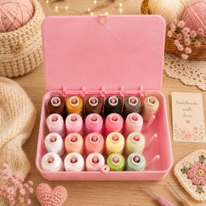 May include: A light pink plastic storage box containing twenty spools of sewing thread in various colors, including shades of pink, white, yellow, green, brown, and black. The box features a hinged lid and vertical pegs to hold each spool upright.