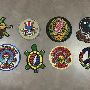 May include: Eight embroidered patches featuring various designs including a green turtle, a skull with a top hat, a yellow skull with floral accents, a skull with a globe, a Grateful Dead logo, a turtle with a lightning bolt, and a peace sign.