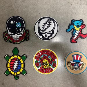 May include: Six embroidered patches featuring Grateful Dead imagery. Designs include a skull with roses and space, a lightning bolt skull, a dancing bear, a turtle with a lightning shell, a bear with roses, and a skull wearing a red, white, and blue top hat.