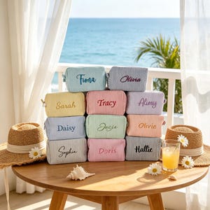 May include: A collection of ten rectangular zipped pouches in various pastel colours, each featuring a fine pinstripe pattern and a unique name embroidered in cursive script, including Fiona, Olivia, Sarah, Tracy, Alimy, Daisy, Josie, Olivie, Sophia, Doris, and Hattie.