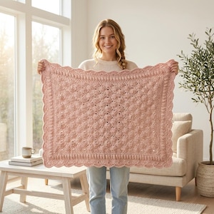 Puede incluir: Una manta rectangular de ganchillo en color rosa empolvado con un patrón texturizado de puntos de burbuja en el centro. La manta está rematada con un borde decorativo festoneado que enmarca toda la pieza con hilo a juego.