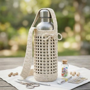 May include: A silver metal water bottle encased in a beige crocheted holder with a grid pattern, a long shoulder strap, and a decorative bow tie at the top. The holder is crafted from light-colored yarn and features a solid base and handle.