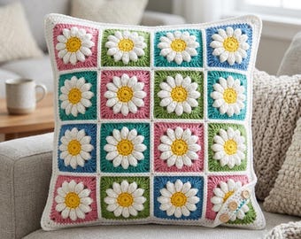 May include: A square crochet pillow cover featuring a grid of sixteen daisy motifs. Each daisy has white petals and a yellow center, set against alternating square backgrounds of pink, green, blue, and teal. Three small wooden buttons are on one corner.
