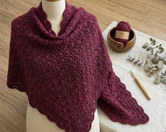 May include: A deep burgundy crochet shawl featuring a textured shell stitch pattern with a scalloped edge. The shawl is draped over a beige mannequin torso, showcasing the intricate yarn work and the triangular shape of the handmade garment.