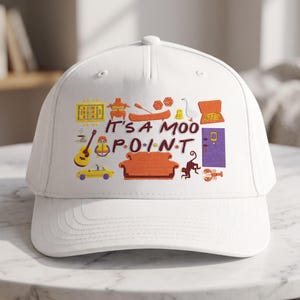 May include: A white baseball cap featuring a colourful embroidered graphic with the text IT'S A MOO POINT. The design includes various icons such as an orange sofa, a yellow taxi, a purple door, a guitar, a monkey, a lobster, and a turkey.