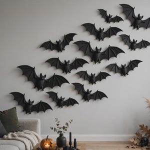 May include: A collection of twelve black bat-shaped wall decorations arranged in a diagonal formation. Each bat features detailed wings and a central body, mounted individually to create a flying effect across the light-colored wall surface.