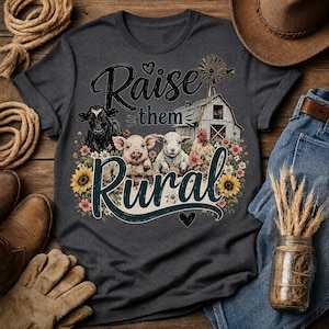 Könnte beinhalten: Ein dunkelgraues T-Shirt mit einem Grafikdruck von einer Kuh, einem Schwein, einem Schaf und einem Huhn vor einer Scheune mit Windmühle. Der Text "Raise them Rural" ist von bunten Blumen und Sonnenblumen umgeben und enthält ein kleines Herz.