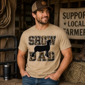 Può includere: Una t-shirt a maniche corte color beige con la scritta SHOW DAD in un motivo mimetico e una sagoma nera di un agnello posizionata tra le parole. Il capo presenta un girocollo ed è realizzato in tessuto a tinta unita.