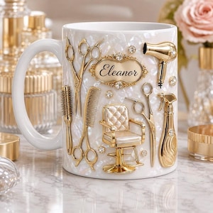 Puede incluir: Una taza blanca con acabado nacarado que presenta herramientas de peluquería doradas en relieve, incluyendo tijeras, un peine, un secador, un pulverizador y un sillón. Una placa dorada central muestra el nombre Eleanor en letra cursiva negra.