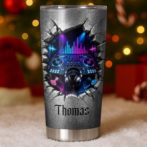 Puede incluir: Un vaso de acero inoxidable con un gráfico de una consola de mezclas de DJ, auriculares y discos de vinilo que parecen romper una pared de piedra gris. El diseño incluye efectos de luz azul y morada vibrantes y el nombre Thomas en negro.
