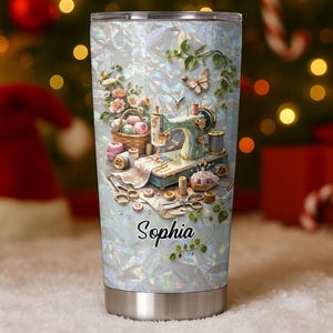 May include: A stainless steel tumbler with a holographic finish featuring a vintage sewing machine, a basket of yarn, scissors, buttons, and a butterfly. The name Sophia is printed in black script on the front of the tumbler, which has a clear lid.