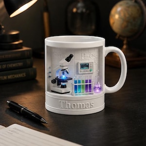 Puede incluir: Una taza de cerámica blanca que presenta una escena de laboratorio tridimensional en su interior. El interior muestra un microscopio en miniatura, un soporte con tubos de ensayo coloridos y un matraz, iluminados con luces LED. El nombre Thomas está en relieve.