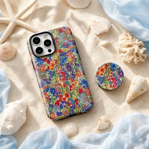May include: A rectangular smartphone case and a matching circular phone grip, both featuring a dense, colourful floral pattern with red, blue, yellow, and green blossoms against a light background, arranged with various seashells on sand.