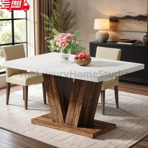 May include: A rectangular dining table with a white top and a dark brown wood grain V-shaped pedestal base. The table is accompanied by two beige upholstered chairs. A glass vase with pink flowers and a bowl of red pomegranates sit on the table.