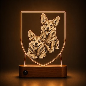 May include: An illuminated acrylic lamp featuring a shield-shaped panel with an etched design of two Corgi dogs. The panel glows with a warm orange light and is mounted on a rectangular wooden base with a small circular power switch on the front.