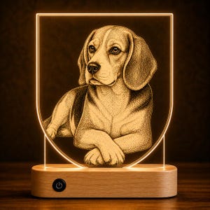 Puede incluir: Una lámpara LED brillante con una ilustración grabada detallada de un perro beagle. El panel de luz tiene forma de escudo con una iluminación ámbar cálida, montado sobre una base rectangular de madera clara con un botón de encendido negro.