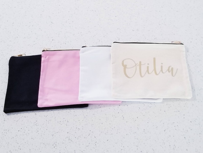 May include: Four zippered pouches in black, pink, white, and beige. The beige pouch has the name "Otilia" written in gold script.