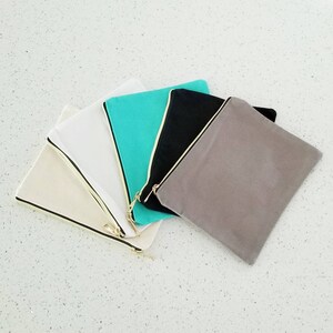 May include: Five canvas zipper pouches in different colors: beige, white, turquoise, black, and gray. The pouches are arranged in a fan shape with the zippers facing outwards.