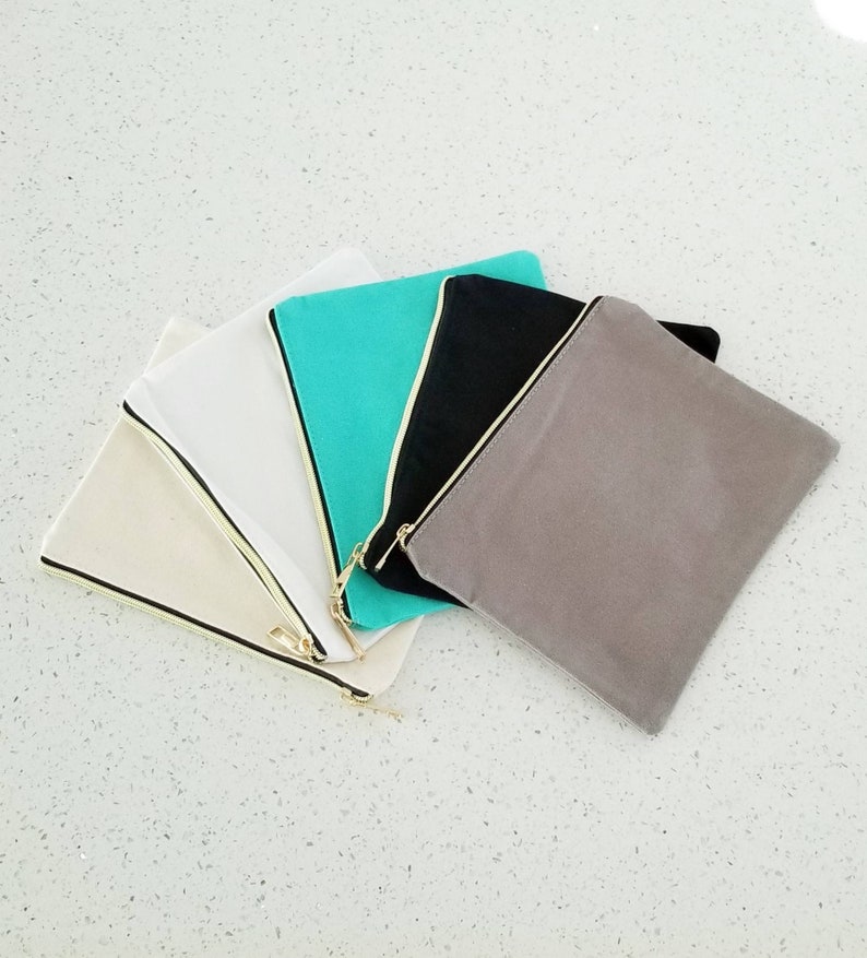 May include: Five canvas zipper pouches in different colors: beige, white, turquoise, black, and gray. The pouches are arranged in a fan shape with the zippers facing outwards.
