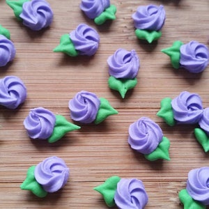 K&ouml;nnte beinhalten: Lila und gr&uuml;ne Zuckerblumen-Dekorationen. Die Blumen sind aus Zuckerguss und haben ein Spiraldesign. Sie sind auf einer Holzoberfl&auml;che angeordnet.