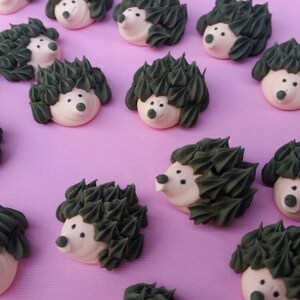 Puede incluir: Una colecci&oacute;n de golosinas con forma de erizo, con espaldas puntiagudas de color verde oscuro y caras claras. Las golosinas est&aacute;n dispuestas sobre una superficie rosa, creando una escena caprichosa y juguetona. Ideales para decoraci&oacute;n o como golosinas.