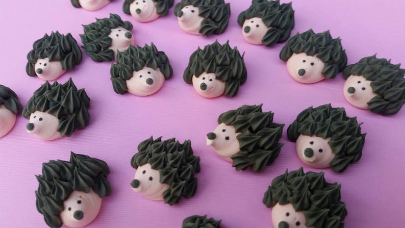Puede incluir: Una colecci&oacute;n de golosinas con forma de erizo, con espaldas puntiagudas de color verde oscuro y caras claras. Las golosinas est&aacute;n dispuestas sobre una superficie rosa, creando una escena caprichosa y juguetona. Ideales para decoraci&oacute;n o como golosinas.