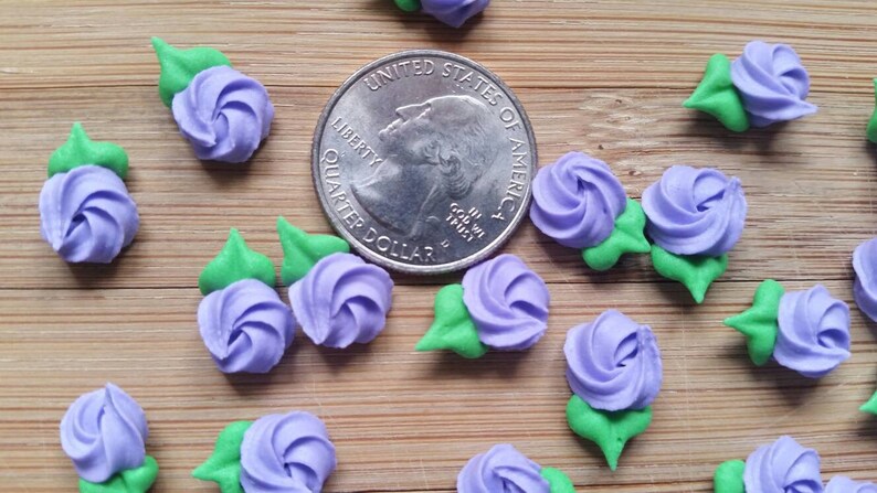 K&ouml;nnte beinhalten: Nahaufnahme einer Gruppe von lila und gr&uuml;nen Zuckerblumen-Dekorationen. Die Blumen sind etwa so gro&szlig; wie eine US-amerikanische 25-Cent-M&uuml;nze.