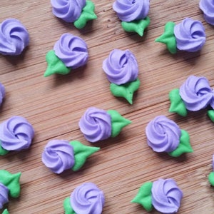 K&ouml;nnte beinhalten: Eine Sammlung von lila und gr&uuml;nen Zuckerblumen, perfekt zum Dekorieren von Kuchen und Cupcakes.