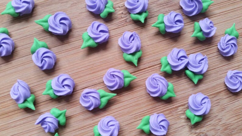 K&ouml;nnte beinhalten: Eine Sammlung von lila und gr&uuml;nen Zuckerblumen, perfekt zum Dekorieren von Kuchen und Cupcakes.