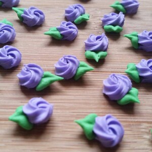 K&ouml;nnte beinhalten: Eine Sammlung von lila und gr&uuml;nen Zuckerrosen, perfekt zum Dekorieren von Kuchen und Cupcakes.