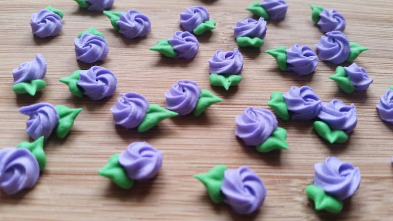 K&ouml;nnte beinhalten: Eine Sammlung von lila und gr&uuml;nen Zuckerrosen, perfekt zum Dekorieren von Kuchen und Cupcakes.