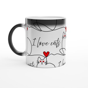 May include: A white ceramic mug featuring a repeating black line art pattern of cats with red heart-shaped eyes. The text "I love cats" is printed in a black script font, interspersed with small red hearts. The mug has a black handle and rim.