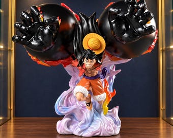 Puede incluir: Una figura de anime dinámica de un personaje con cabello negro y sombrero de paja, vistiendo un chaleco rojo abierto y pantalones cortos naranjas. La figura presenta dos puños negros brillantes de gran tamaño y humo púrpura y blanco.