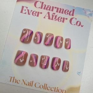 May include: A set of ten press-on nails featuring a nude base with wavy pink and purple stripes and small white mouse-ear silhouettes. The display card is printed with the text Charmed Ever After Co. and The Nail Collection.