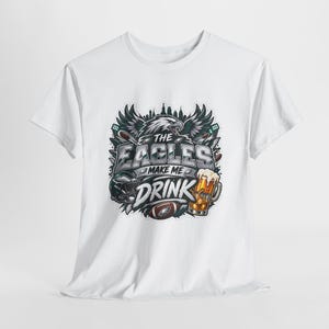 Pode incluir: Uma t-shirt branca de manga curta com uma estampa gráfica de uma águia, um capacete de futebol americano, uma bola e uma caneca de cerveja. O texto THE EAGLES MAKE ME DRINK está escrito em letras arrojadas e estilizadas.