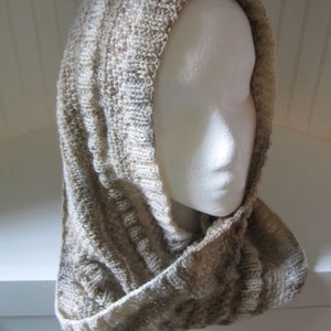 May include: A beige and white knitted cowl neck scarf with a hood. The scarf is made of a soft, textured yarn and is perfect for keeping warm in the winter.