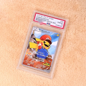 Könnte beinhalten: Eine Pokemon-Sammelkarte aus dem Jahr 2016 mit Pikachu als Mario verkleidet, eingeschlossen in einer transparenten PSA-bewerteten Kunststoffhülle. Die Karte zeigt die Figur mit roter Mütze, blauer Latzhose und Schnurrbart sowie japanischem Text.