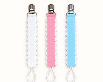 May include: Three dummy clips with the text CSRA Stitch & Press above them. Each clip features a silver metal clasp, a white, pink, or light blue ribbon centre with scalloped white edges, and a white elastic loop at the bottom for attachment.