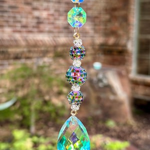 May include: A hanging suncatcher ornament featuring two faceted yellow and blue octagonal crystals, three iridescent disco ball beads separated by small silver spacers, and a large, teardrop-shaped blue and green faceted crystal pendant.