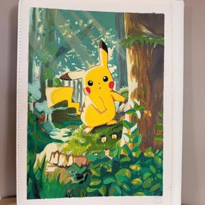 Puede incluir: Una pintura rectangular sobre una cubierta de carpeta blanca que muestra a un personaje Pikachu amarillo de pie sobre una roca cubierta de musgo en un bosque. La escena incluye un gran tronco de árbol marrón, follaje verde y luz filtrada.