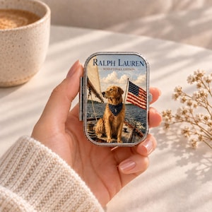 May include: A rectangular metal tin featuring a printed image of a golden retriever wearing a dark blue bandana on a sailboat. The text RALPH LAUREN MINNETONKA EDITION is printed in dark blue at the top. The tin has a silver-toned metal frame.