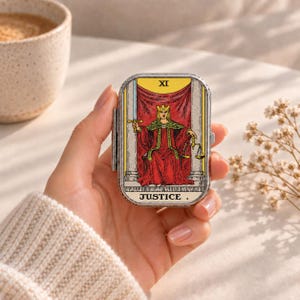 May include: A rectangular metal tin featuring the Justice tarot card design on the lid. The illustration depicts a crowned figure in a red robe holding a sword and scales, with the Roman numeral XI and the word JUSTICE printed on the front.