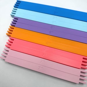 Può includere: Un set di dieci barre rettangolari in plastica per telaio in vari colori, tra cui blu, azzurro, viola, arancione, rosa e rosa chiaro. Ogni barra presenta estremità dentellate ed è impressa con la sua lunghezza in pollici, da 7 a 9.