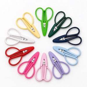 May include: A collection of ten small, spring-loaded thread snips arranged in a circle. Each pair of scissors features a distinct solid color, including yellow, green, dark green, navy blue, light blue, purple, light pink, hot pink, red, and white.