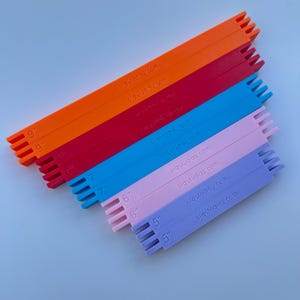 May include: A set of six rectangular plastic bars in orange, red, blue, pink, light pink, and purple. Each bar features slotted ends and is embossed with the text srqstudios.com and specific measurements of 9, 7, 6, and 5 inches respectively.